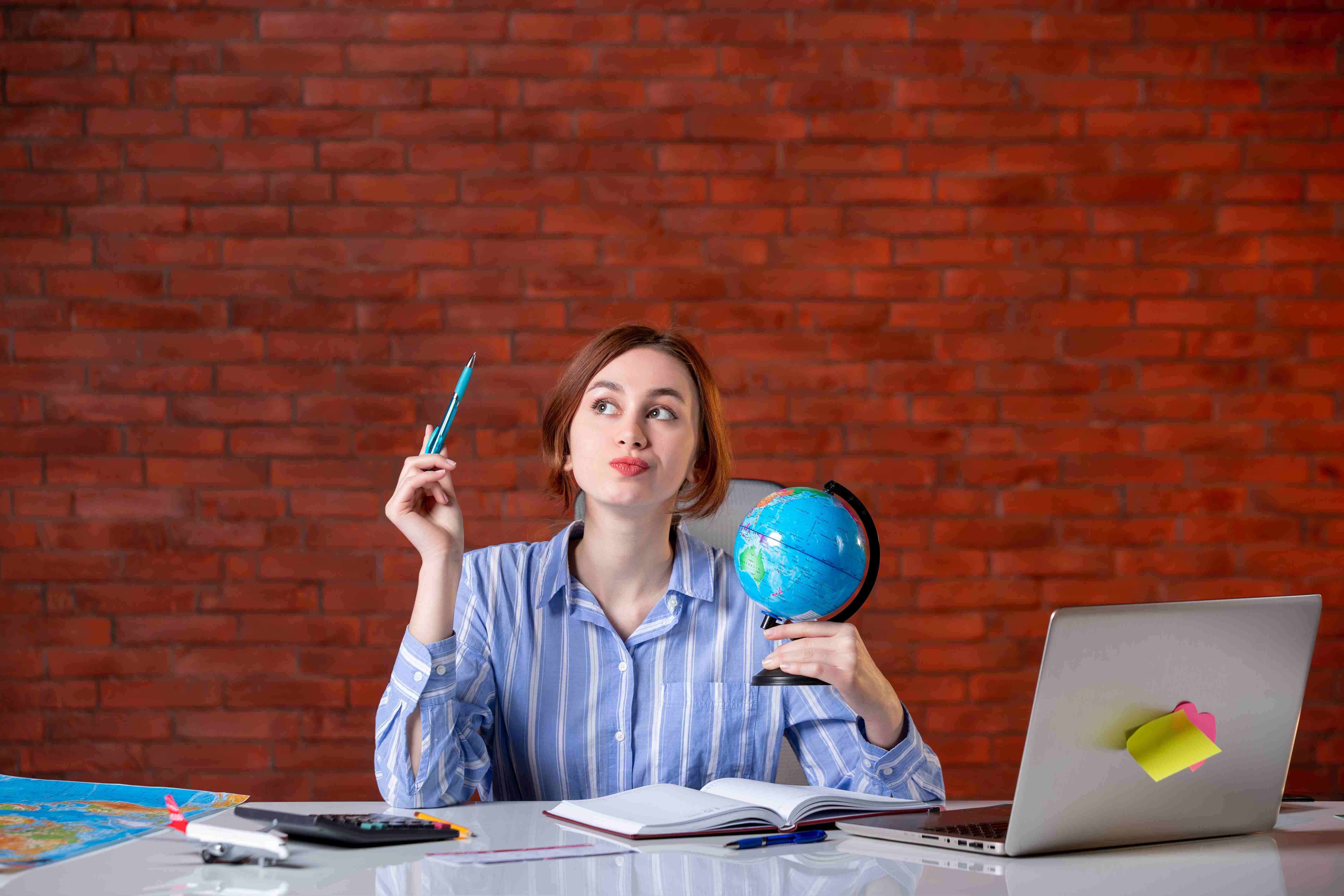 A girl sits at a desk with a globe and a pencil, contemplating studying abroad.